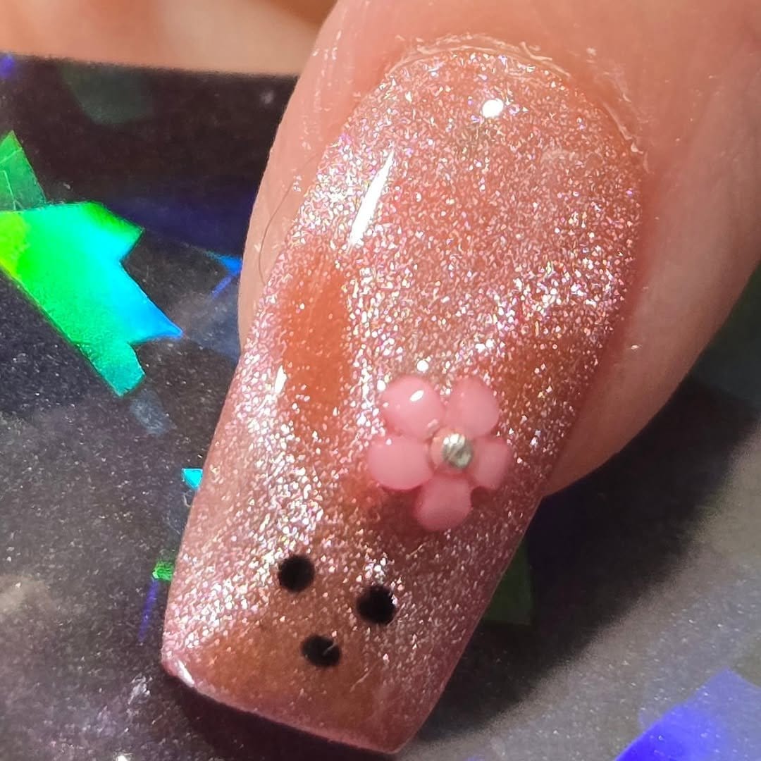 Glitter nail art resembling dewdrops on a pink background