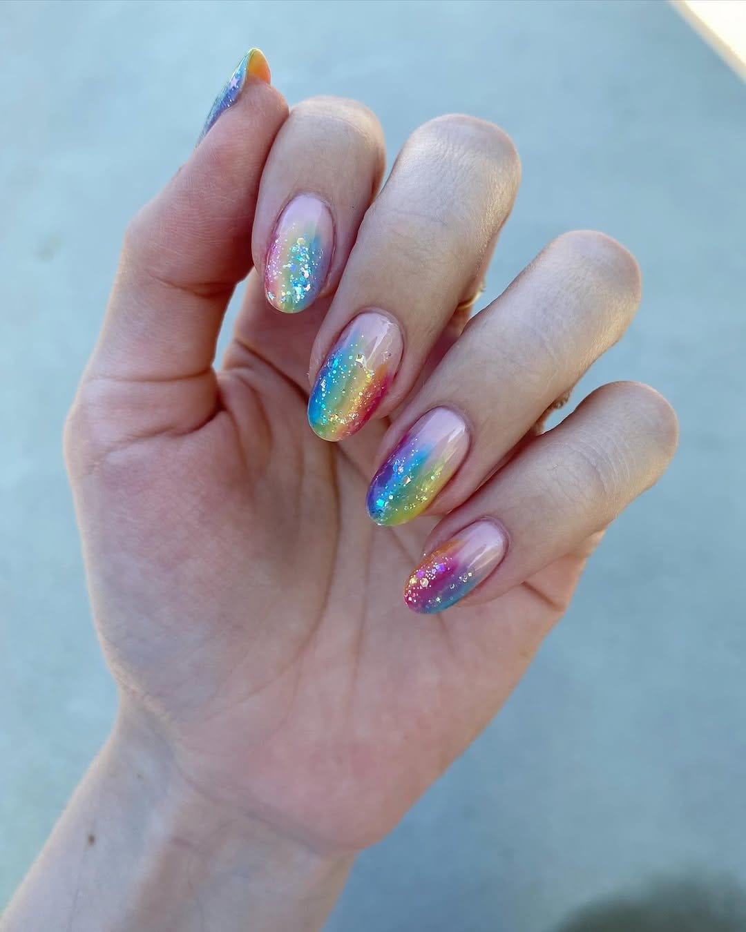 Vibrant pastel rainbow ombre nails with a sunset backdrop